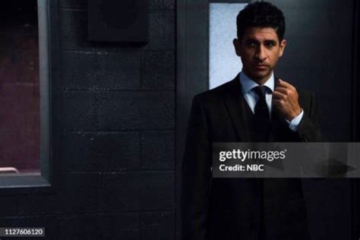 Raza Jaffrey in black formal dress posing with his wife Lara Pulver in a grey bodycon and golden jewelry.